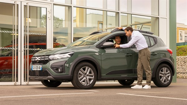 Dacia parkirana ispred prodajnog salona, dok djelatnik razgovara s vozačem kroz otvoreni prozor vozila.