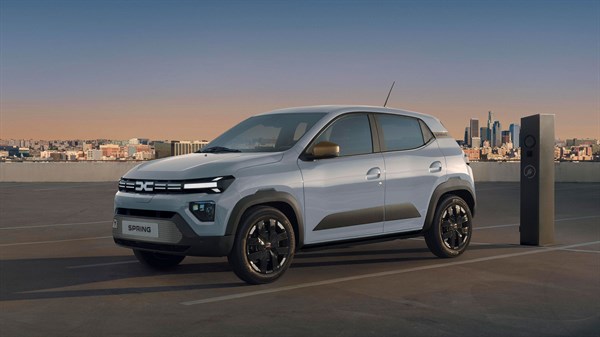 Bijelo vozilo Dacia Spring iz bočnog profila pod nadstrešnicom parkirališta, uz stanicu za punjenje.