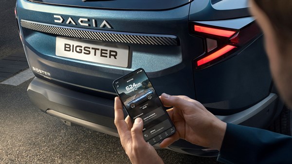 Stražnji dio vozila Dacia Bigster dok korisnik putem mobilne aplikacije upravlja funkcijama vozila na pametnom telefonu.