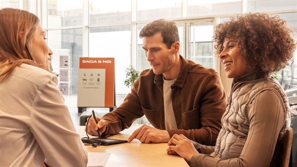 Dvoje klijenata sjede za stolom i razgovaraju s djelatnicom Dacije u modernom salonu.







