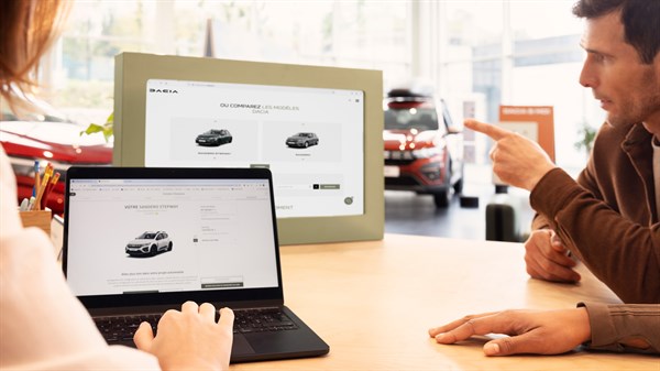 Dvoje ljudi sjedi za stolom u salonu i pregledava ponudu vozila Dacia na prijenosnom računalu.