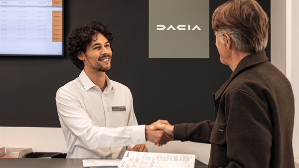 Osoba u odijelu rukuje se s Dacia savjetnikom za pultom u salonu, u poslovnom ambijentu.

