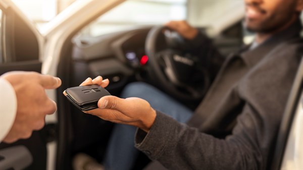 Vozač sjedi u vozilu i prima ključ od druge osobe kroz otvorena vrata automobila.







