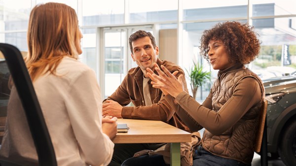 Dvoje klijenata sjede za stolom i razgovaraju s djelatnicom Dacije u modernom salonu.







