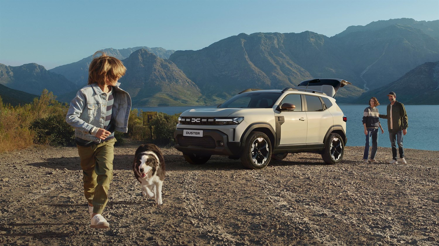 Vozilo Dacia Duster parkirano uz jezero i planinski krajolik, s obitelji i psom u prirodi.