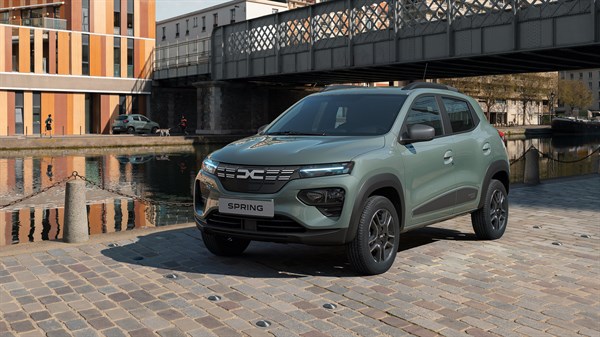 Dacia Spring Electric parkirana na otvorenom parkiralištu pored punionice, s panoramom grada u pozadini.