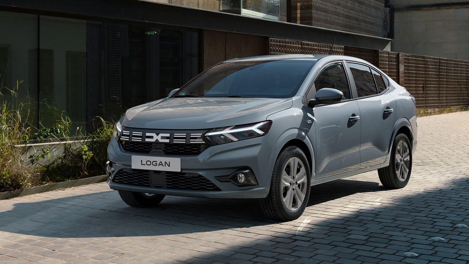 Sivi Dacia Logan parkiran ispred moderne stambene zgrade.