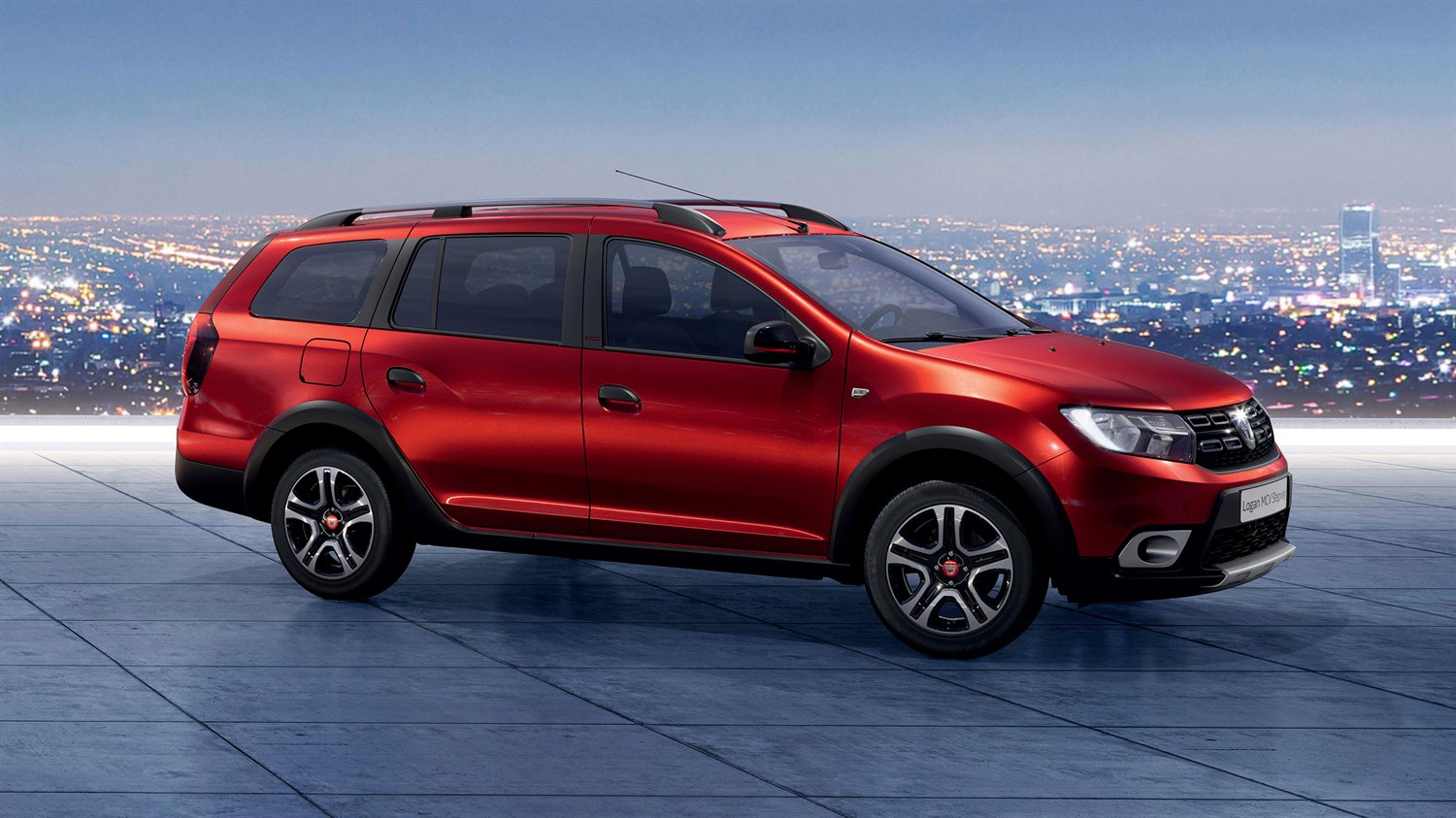 Crveni Dacia Logan MCV prikazan iz bočnog kuta na urbanoj pozadini.