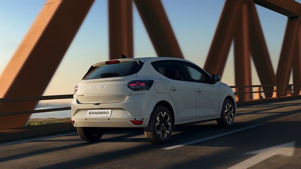 Bijeli Dacia Sandero u vožnji preko mosta, snimljen sa stražnje bočne strane.