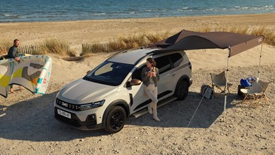 Bijeli Dacia Jogger parkiran na plaži s otvorenom tendom i opremom za odmor.