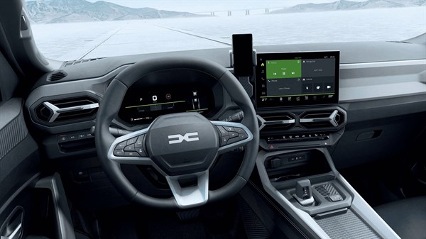 Interijer vozila Dacia s upravljačem, digitalnom instrumentnom pločom i središnjim multimedijskim zaslonom, snimljen u zimskom krajoliku.