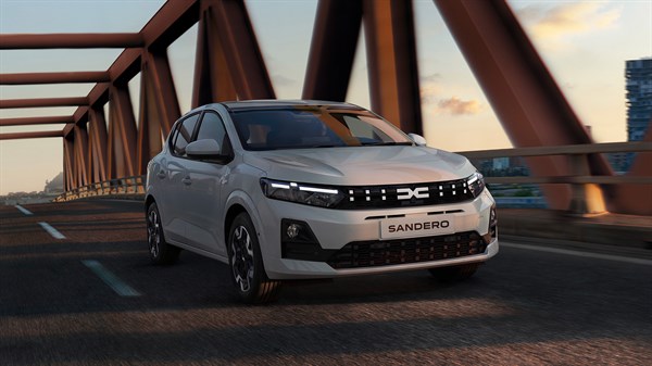 Srebrna Dacia Sandero u vožnji preko gradskog mosta u suton