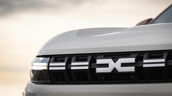 Detalj prednje maske bijelog vozila Dacia s prepoznatljivim logotipom na središnjem dijelu.