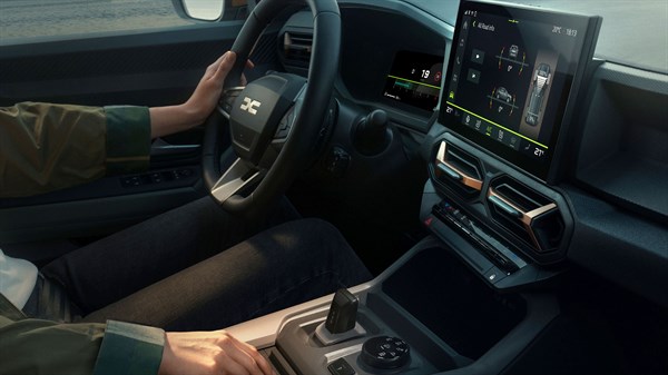 Vozač u Dacia vozilu s digitalnom instrumentnom pločom, središnjim dodirnim zaslonom i automatskim mjenjačem.