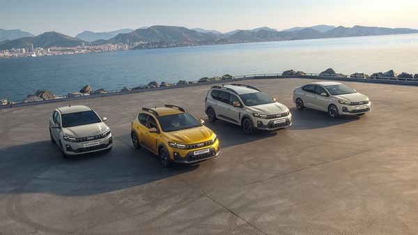 Četiri Dacia vozila parkirana uz morsku obalu na prostranom platou, s pogledom na more, planine i grad u pozadini.