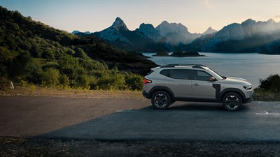 Vozilo Dacia Duster parkirano uz jezero, s planinama u pozadini.