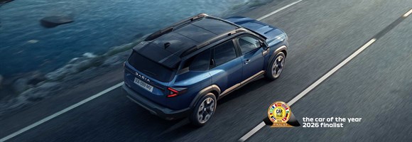 Plavo vozilo Dacia Bigster u vožnji autocestom uz obalu, snimljeno iz ptičje perspektive.