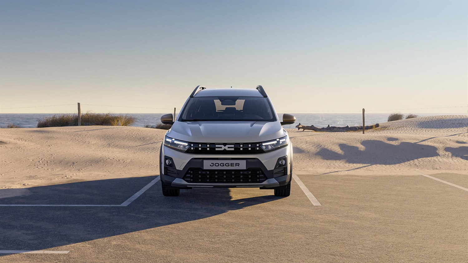 Vozilo Dacia Jogger snimljeno sprijeda na parkiralištu uz pješčanu plažu i more.