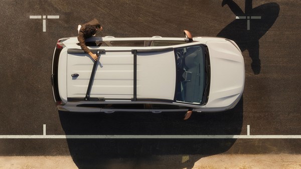 Vozilo Dacia Jogger snimljeno odozgo na parkiralištu s krovnim nosačima i osobom koja stoji pokraj vozila.