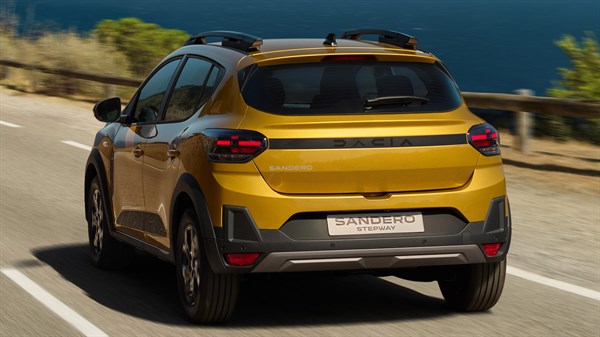 Stražnji pogled na vozilo Dacia Sandero Stepway u zlatnoj boji koje vozi uz obalu s plavim morem u pozadini.