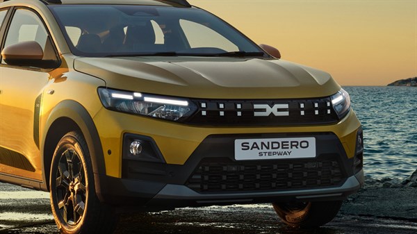 Prednji dio vozila Dacia Sandero Stepway u zlatnoj boji, snimljen u vožnji uz obalu pri zalasku sunca.