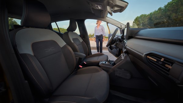 Pogled u unutrašnjost vozila Dacia Sandero Stepway kroz otvorena vrata, s osobom koja stoji ispred vozila na suncu.