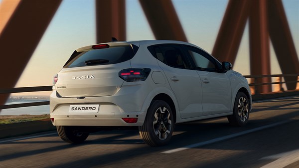 Stražnji dio vozila Dacia Sandero u bijeloj boji koje prelazi most pri zalasku sunca.