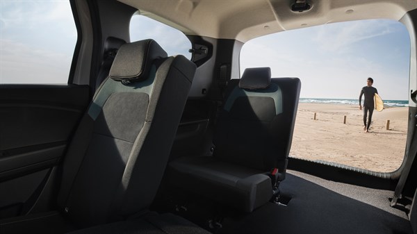 Pogled iz unutrašnjosti vozila Dacia Jogger prema otvorenim stražnjim vratima, kroz koja se vidi osoba kako hoda po plaži uz more.
