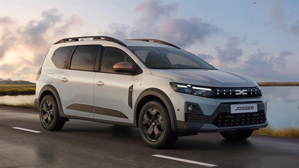 Vozilo Dacia Jogger u bijeloj boji vozi se uz obalu pri zalasku sunca.