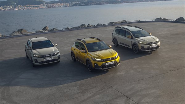 Tri vozila – Dacia Sandero, Dacia Sandero Stepway i vozilo Dacia Jogger – parkirana uz obalu s pogledom na more i grad u pozadini.