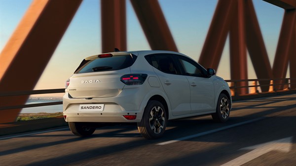 Vozilo Dacia Sandero u bijeloj boji snimljeno straga u vožnji preko metalnog mosta, s naglašenim novim stražnjim svjetlima i linijama karoserije.