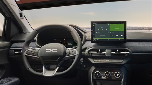 Unutrašnjost vozila Dacia s prikazom upravljača, multimedijalnog zaslona i vozačkih vrata, dok muškarac stoji vani pokraj otvorenih vrata.








