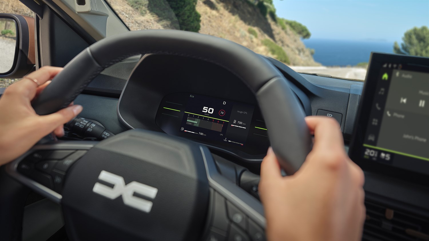 Vozač drži upravljač u vozilu Dacia Sandero, a na digitalnoj instrument ploči prikazane su informacije o brzini, dosegu i načinu vožnje.