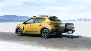 Žuto vozilo Dacia Sandero prikazano sa stražnje strane na otvorenoj cesti, s prikolicom pričvršćenom na kuku za vuču.