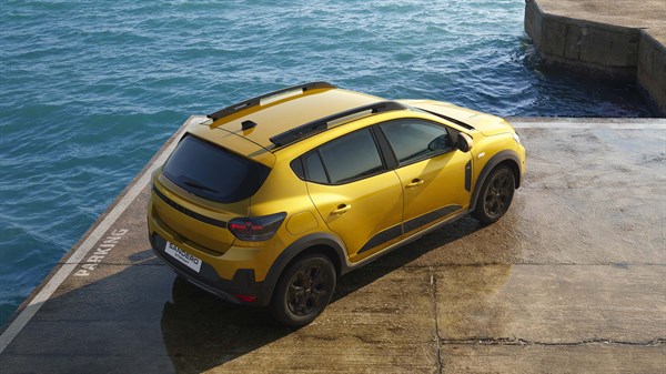 Vozilo Dacia Sandero u žutoj boji snimljeno odozgo, parkirano uz more na betonskoj površini.