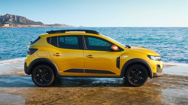 Vozilo Dacia Sandero Stepway u žutoj boji snimljeno iz profila uz morsku obalu, parkirano na mokroj betonskoj površini.