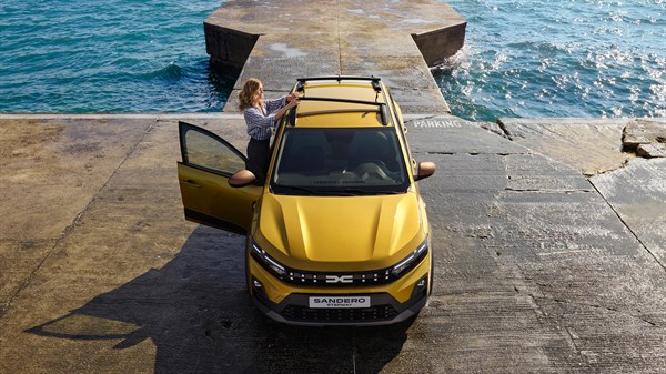 Vozilo Dacia Sandero Stepway snimljeno odozgo uz more, s otvorenim vratima i modularnim krovnim nosačima na krovu.