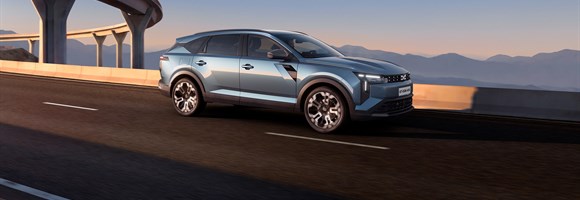 Dacia Striker prikazan iz bočnog profila u vožnji cestom, uz moderan arhitektonski objekt i zalazak sunca u pozadini.