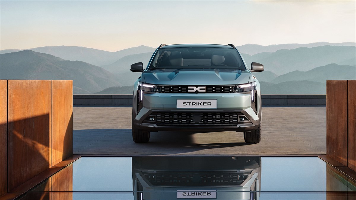 Vozilo Dacia Striker snimljeno sprijeda na otvorenoj terasi s pogledom na planinski krajolik u pozadini, s naglašenom prednjom maskom, LED svjetlima i modernim dizajnom vozila u mirnom prirodnom okruženju