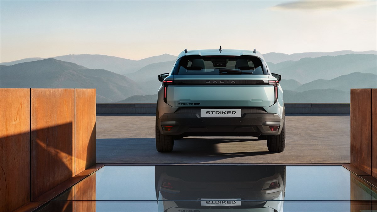 vozilo Dacia Striker snimljeno straga na otvorenoj terasi s pogledom na planine u pozadini, s naglašenom stražnjom LED svjetlosnom linijom, logotipom Dacia i refleksijom vozila na površini vode u prvom planu
