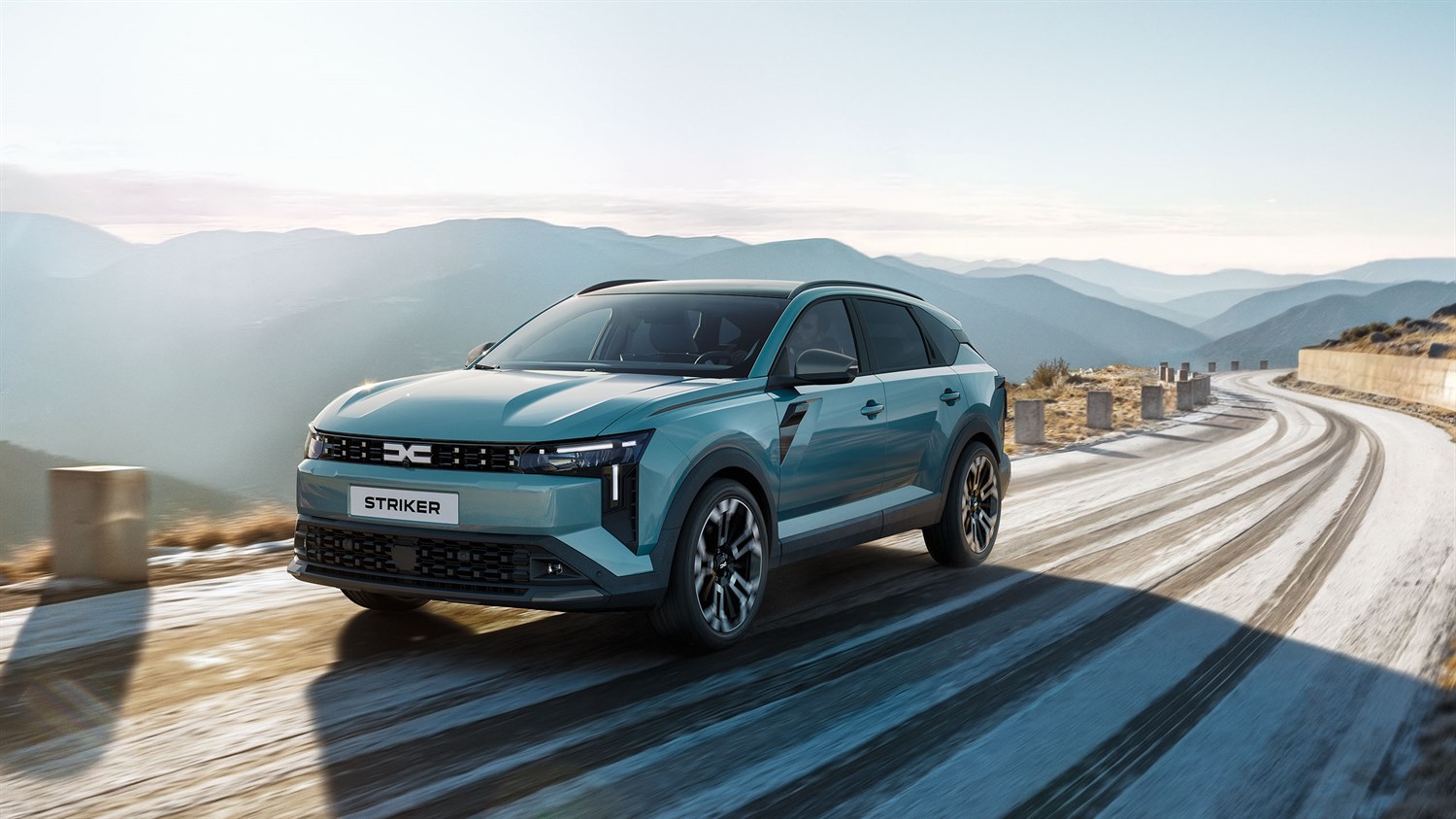 vozilo Dacia Striker vozi zavojitom planinskom cestom uz kamenu ogradu, prikazano iz prednje bočne perspektive s naglašenom prednjom maskom i LED svjetlima, dok se u pozadini pruža panoramski pogled na planinski krajolik