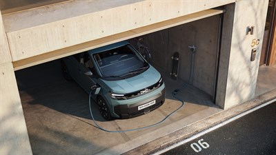 Dacia Spring u svijetloplavoj boji parkiran u garaži, priključen kabelom na zidnu punionicu za električna vozila.