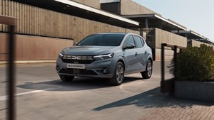 Vozilo Dacia Sandero parkirano ispred moderne zgrade, s otvorenom garažnom ogradom.
