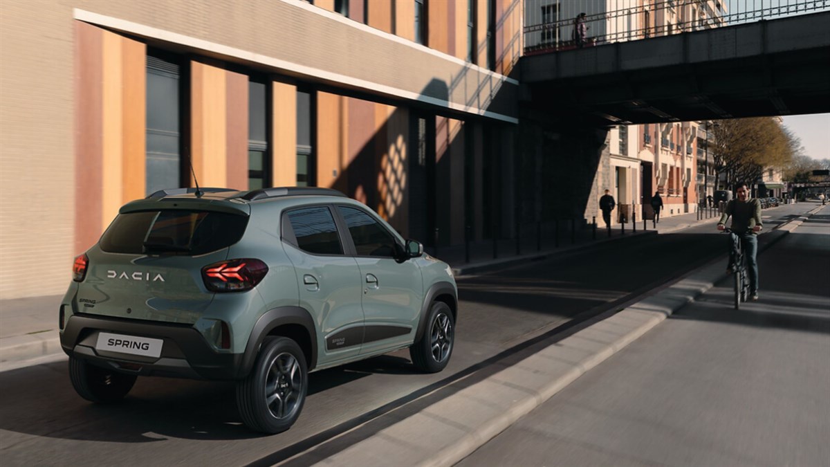 Zelena Dacia Spring Electric parkirana uz rub pločnika ispred zgrade.
